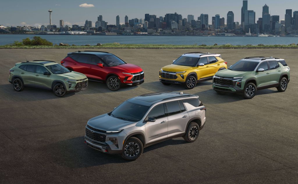 A lineup of five colorful Chevy SUVs parked with a city skyline in the background.